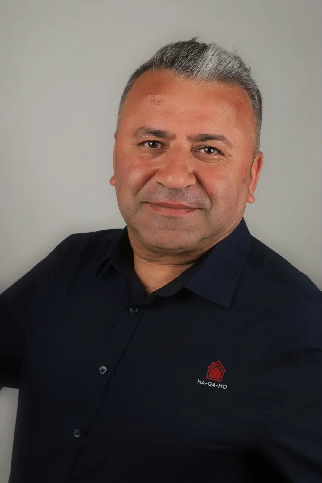 Porträt von Mehmet Özdemir mit dem Firmenlogo auf dem Hemd.