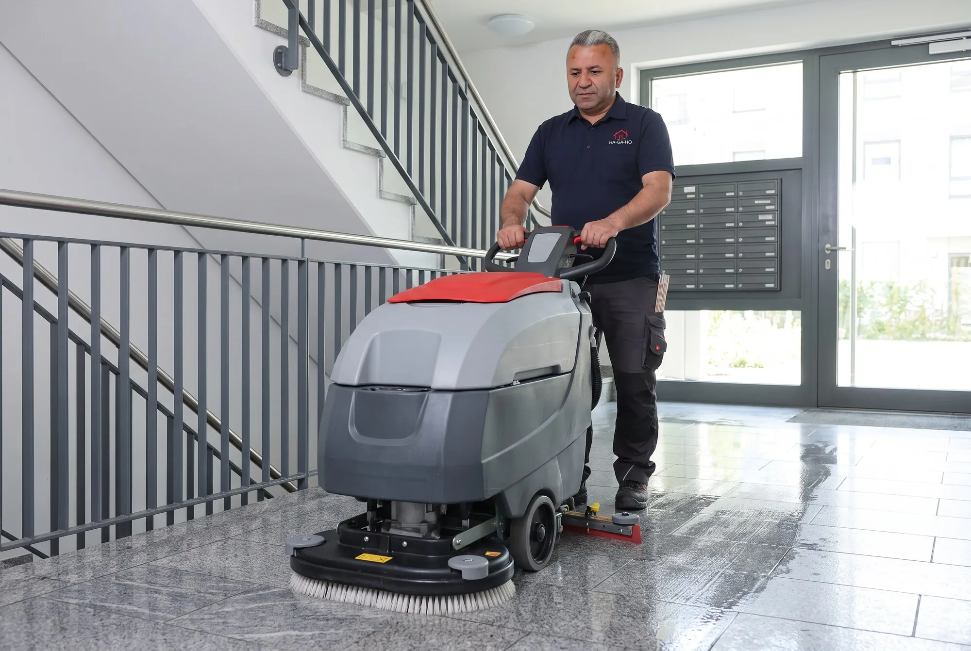Mehmet Özdemir im Hemd mit Firmenlogo reinigt einen Hausflur mit einer großen Scheuersaugmaschine.